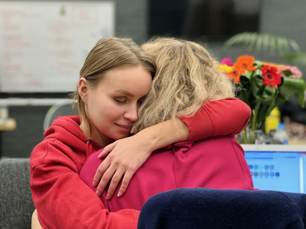 Two women hugging in an office setting, a supportive moment relevant to responding to someone in distress